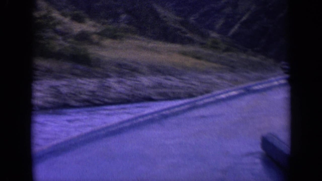 1963 Washington 8mm frame showing a narrow mountain waterway, rippled surface, wake lines, and brushy slopes in a blue-purple color shift.