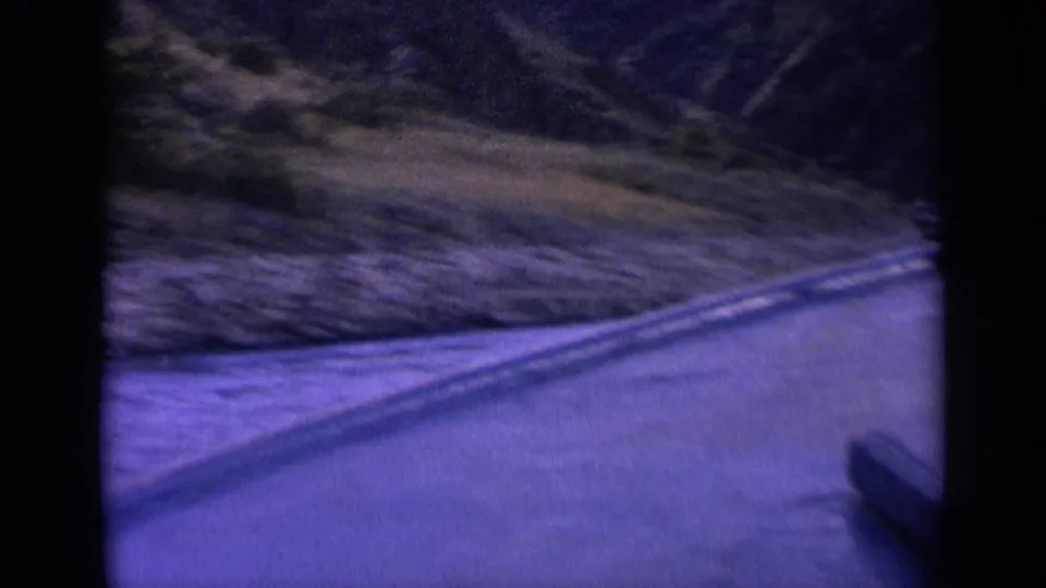 1963 Washington 8mm frame showing a narrow mountain waterway, rippled surface, wake lines, and brushy slopes in a blue-purple color shift.
