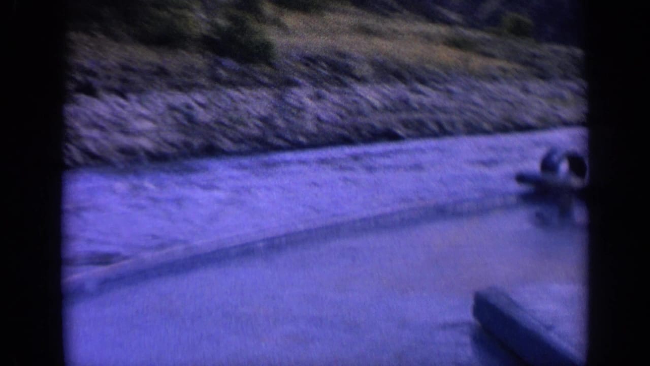 1963 Washington 8mm frame with a small boat ahead on the water, a rippled channel, rocky shore, and dark film-gate edges.