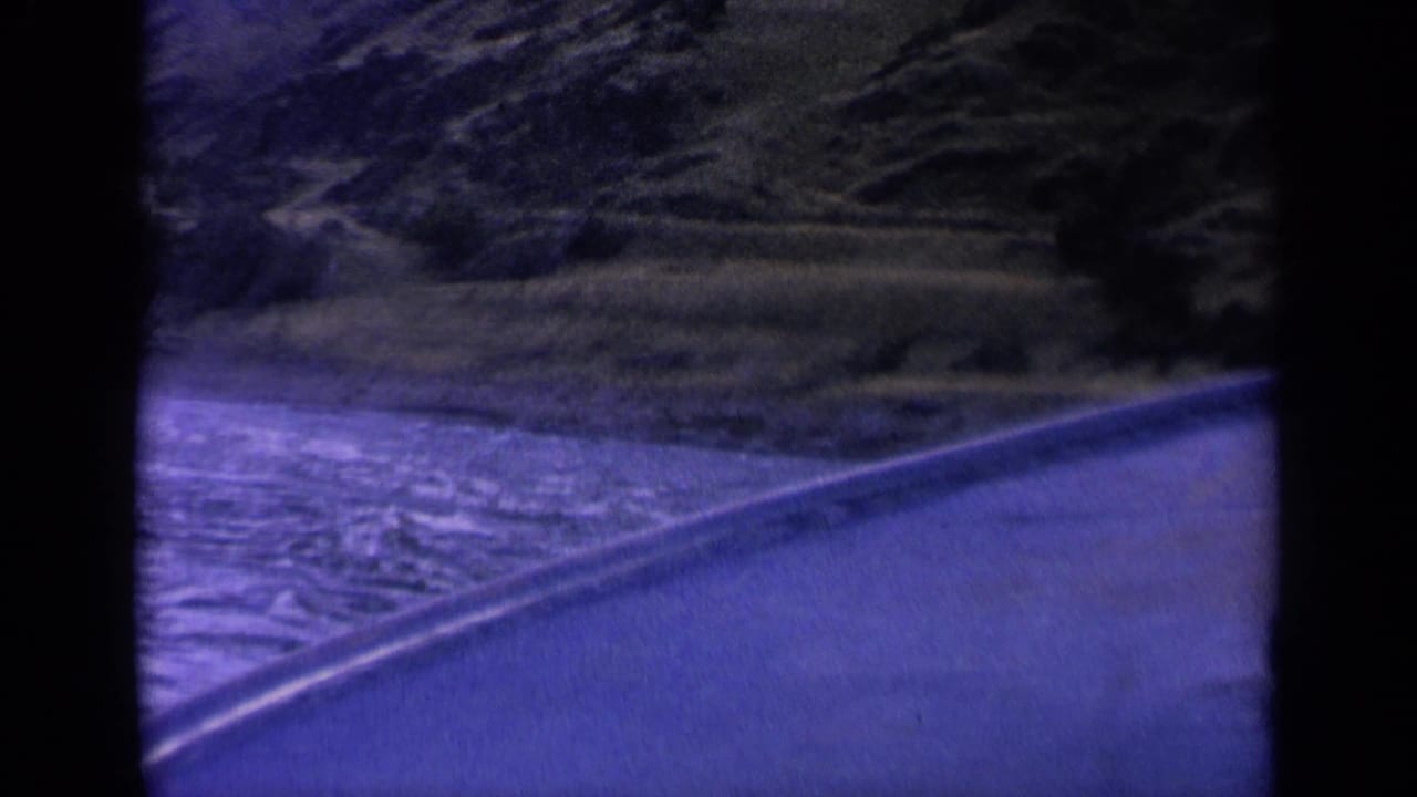 1963 Washington 8mm frame showing a curving wake on a mountain waterway with rocky slopes and sparse vegetation beyond.