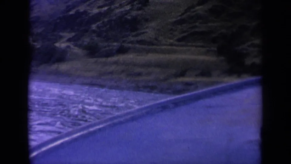 1963 Washington 8mm frame showing a curving wake on a mountain waterway with rocky slopes and sparse vegetation beyond.