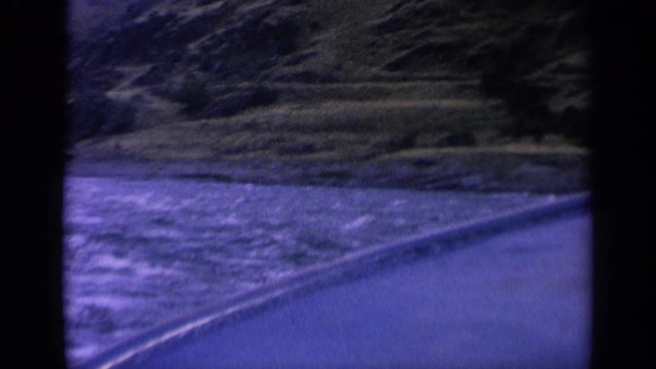 Blue-tinted water and a curving shoreline below dark wooded hills.