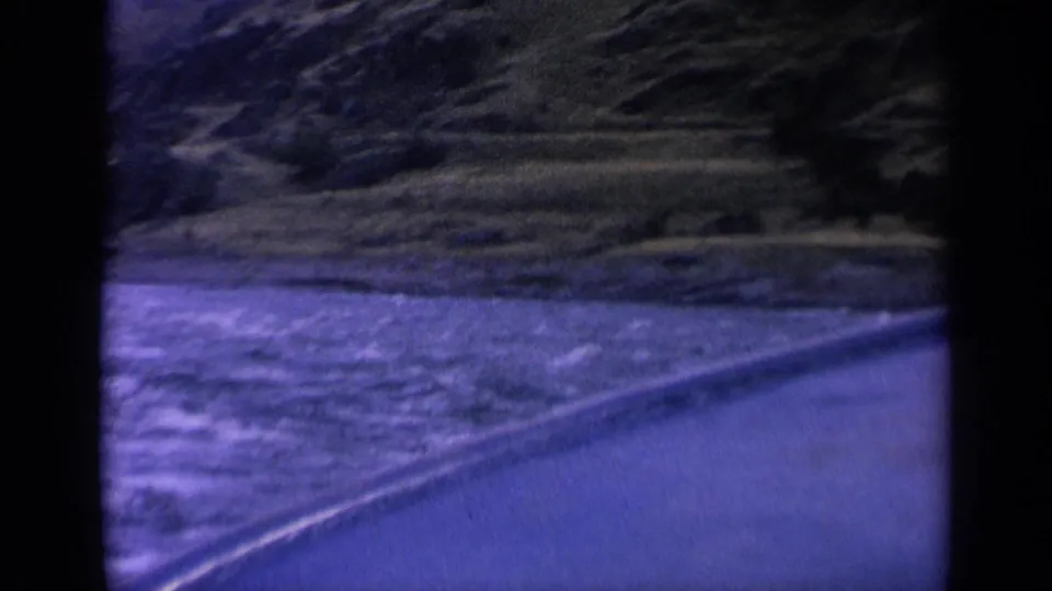 1963 Washington 8mm frame showing rippled water beside a curving bank and dark green hills, with heavy blue color cast.