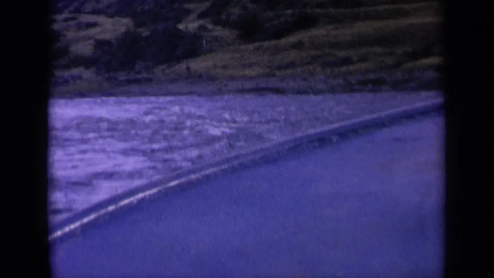 1963 Washington home-movie frame with rippled water, a diagonal shoreline edge, and shadowed hillside greenery.