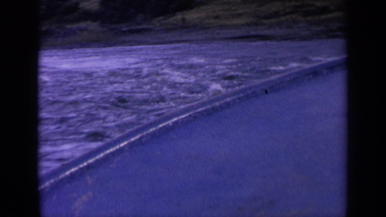 1963 Washington home-movie frame of churning water beside a road or shoreline, seen in soft 8mm color.