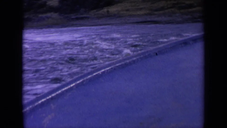 1963 Washington home-movie frame of churning water beside a road or shoreline, seen in soft 8mm color.
