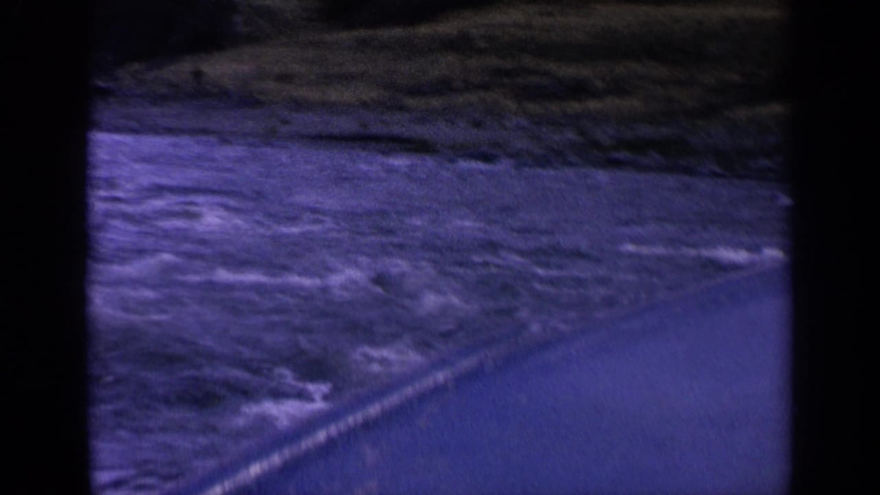 1963 Washington 8mm frame showing turbulent water from a moving boat, with shoreline and a diagonal paved edge visible.