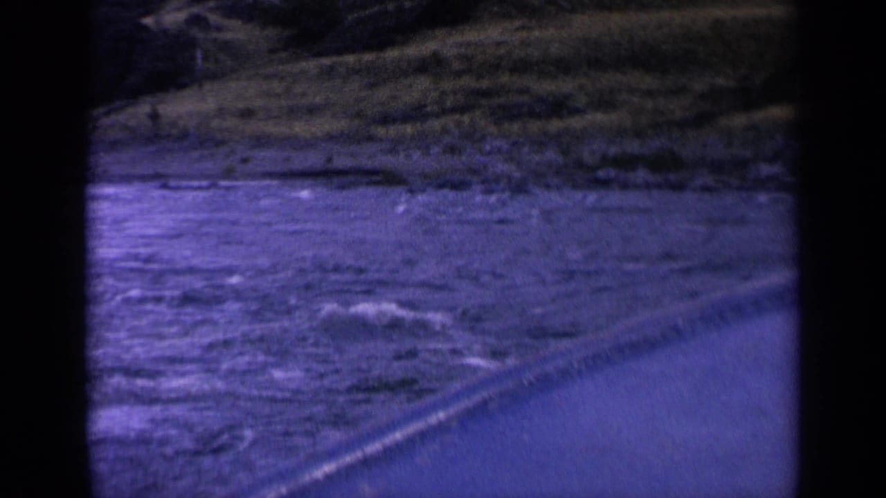 1963 Washington 8mm frame with rippling water, a diagonal edge, and distant grassy shoreline from a moving boat viewpoint.