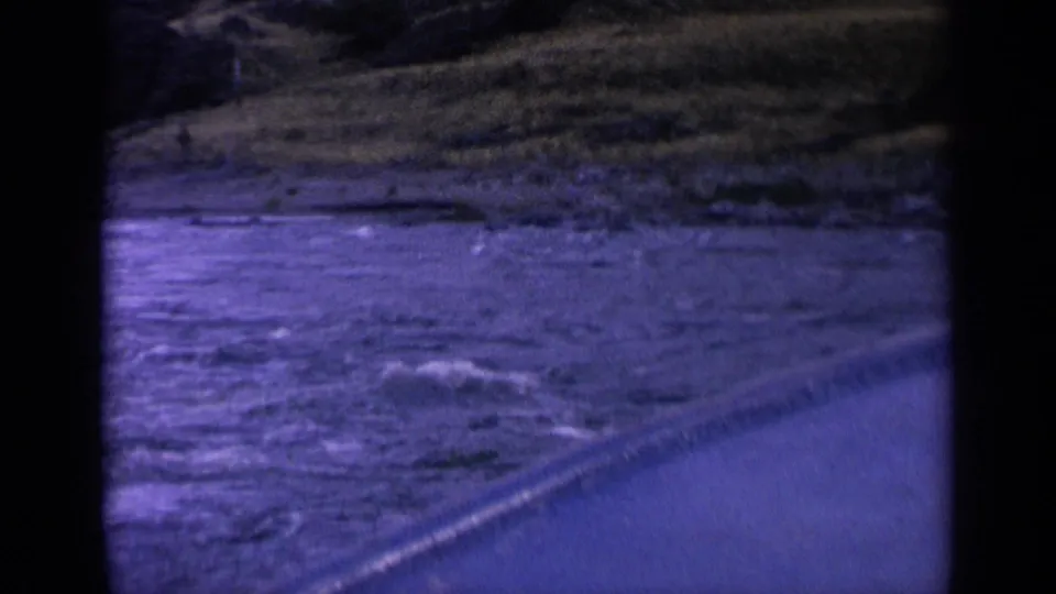 1963 Washington 8mm frame with rippling water, a diagonal edge, and distant grassy shoreline from a moving boat viewpoint.
