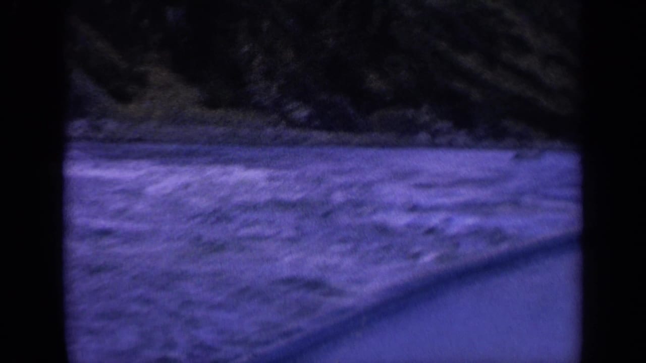 1963 Washington 8mm frame with blurred churning water, dark shoreline, and diagonal foreground edge from a moving boat.