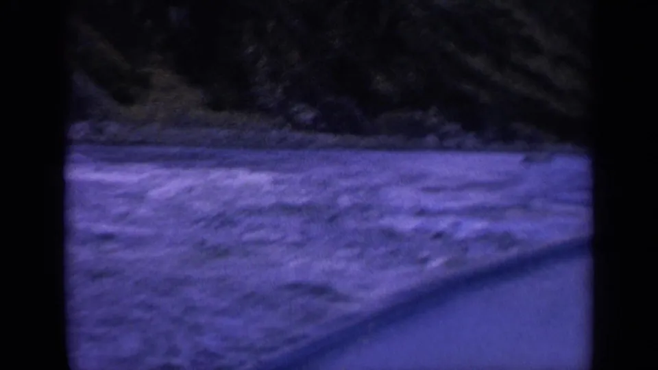 1963 Washington 8mm frame with blurred churning water, dark shoreline, and diagonal foreground edge from a moving boat.