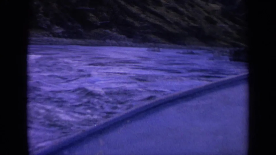 1963 Washington 8mm frame showing churning blue water, a sloped vessel edge, and a dark rocky bank in the background.