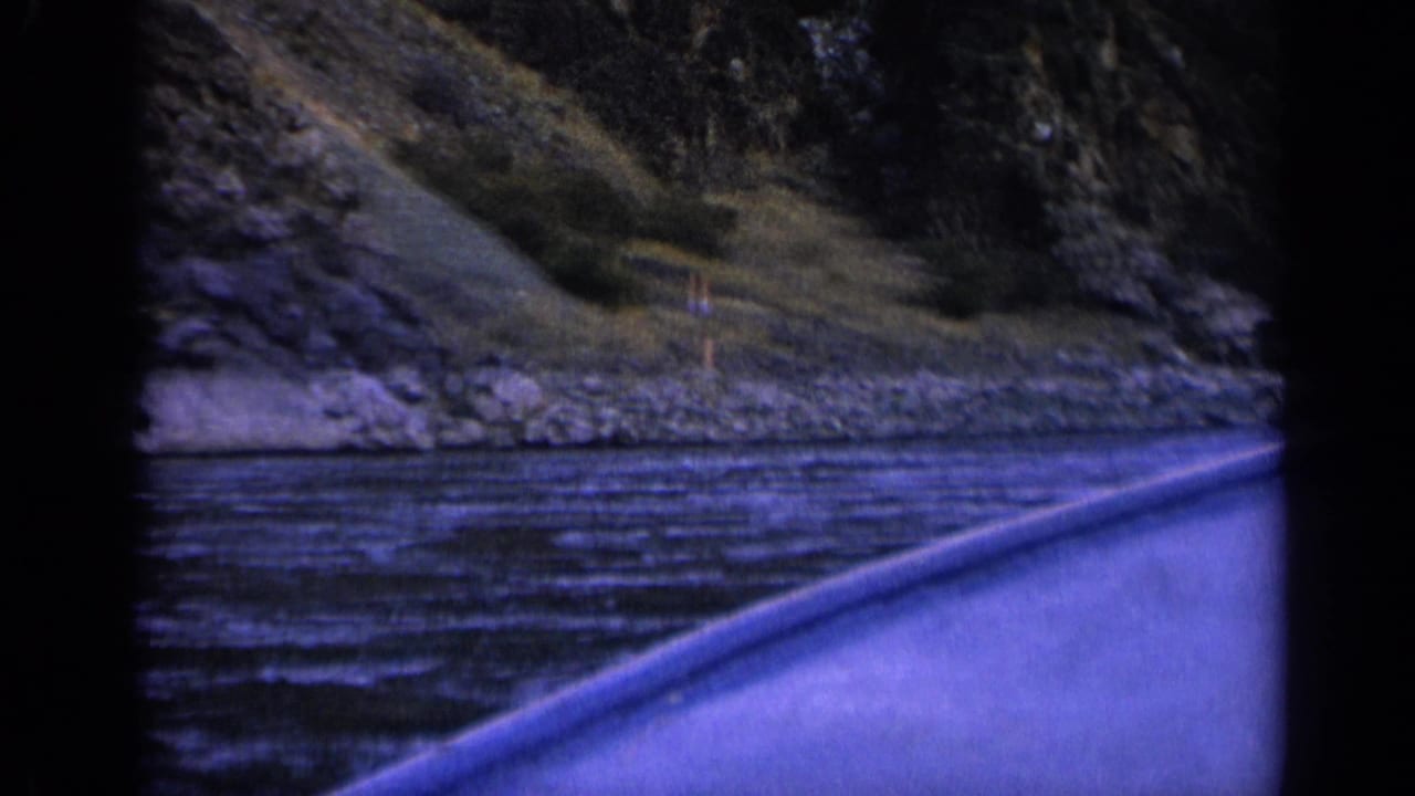 1963 Washington home-movie frame looking from a moving boat across rough river water toward steep canyon walls.