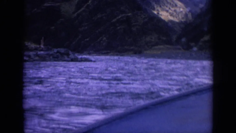 A moving boat passes rough water in a Washington canyon, seen through dark window framing on 8mm film.