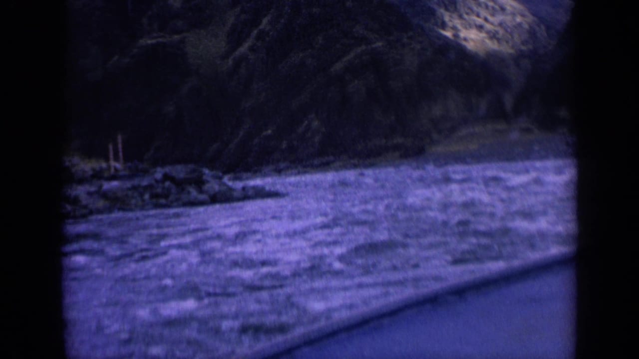 1963 Washington 8mm frame showing a river and rocky bank viewed from a moving vehicle through dark window framing.