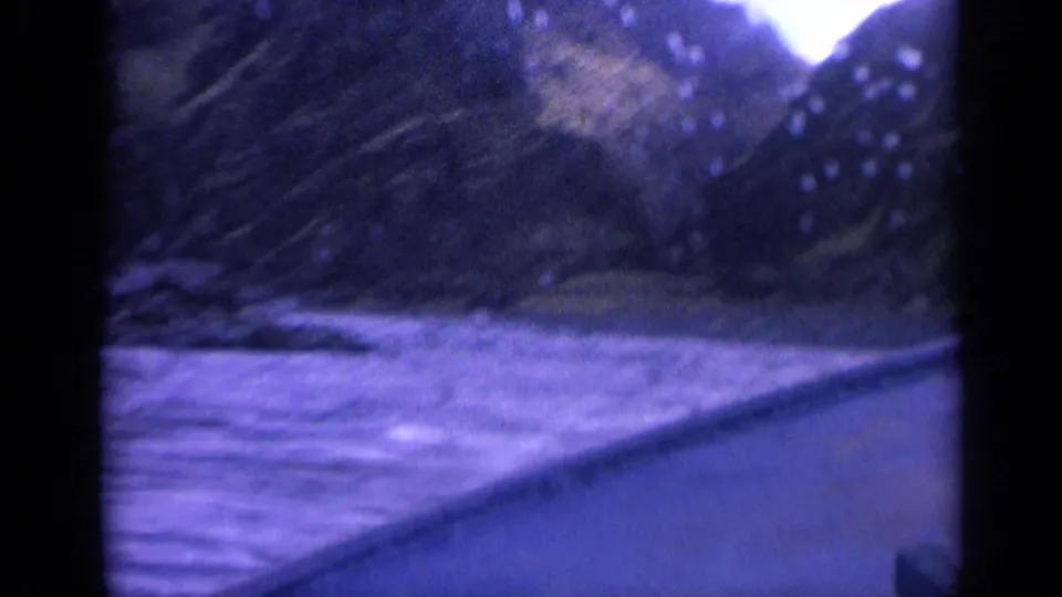 Washington 8mm travel frame showing a river bend, steep slopes, bright overcast sky, and vehicle window framing.