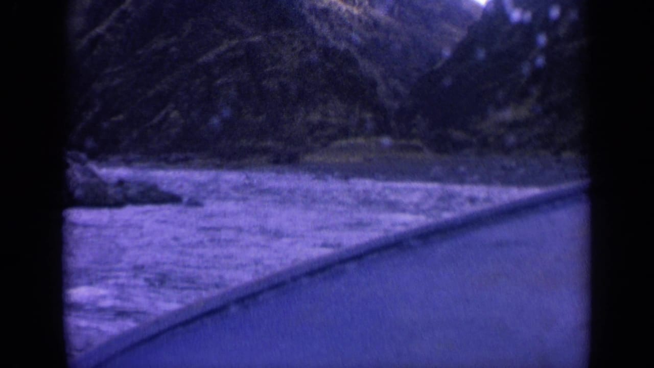 1963 8mm boat-view frame showing rough water, a curved boat edge, and steep wooded slopes in Washington.
