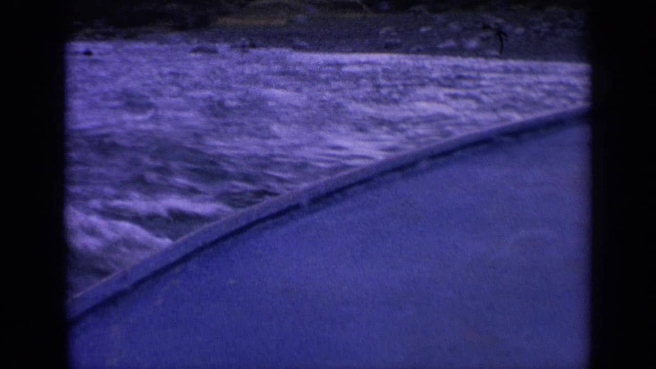 Purple-blue surf beside a concrete or stone shoreline edge under dark film borders.