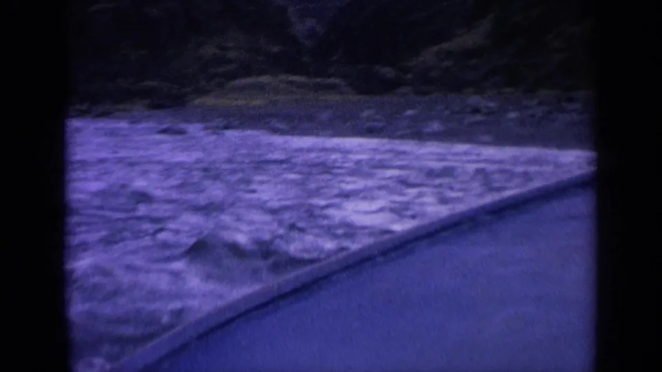 1963 Washington coastal frame with rough ocean water, a sloping concrete or stone edge, and dark rocky shoreline in the background.