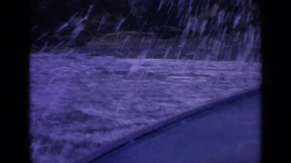 1963 Washington 8mm frame showing spray and rough surf against a shoreline edge, with strong grain and a blue-purple cast.