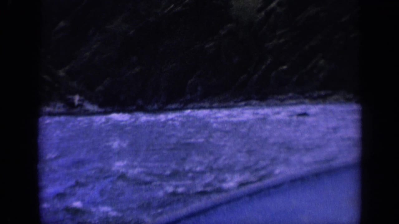 Blue-tinted choppy water beside a curved boat edge with dark shoreline above.