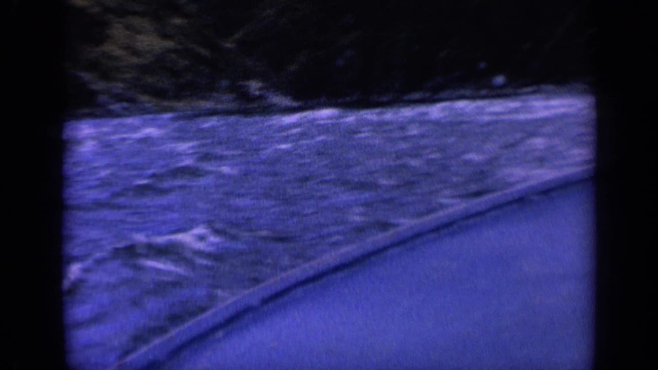 Foamy water surface and a curved boat side with dark land in the background.