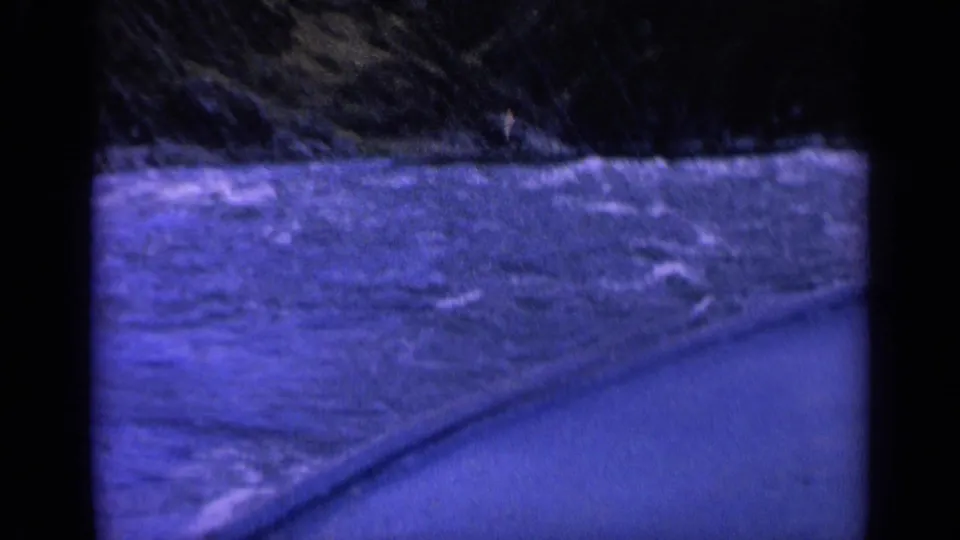 Blue-shifted 8mm frame showing a moving boat edge and churning water near a dark Washington shoreline.