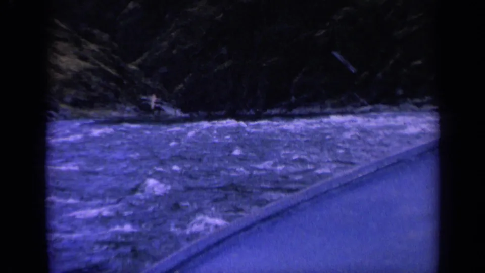 1963 Washington 8mm frame of churning river water beside a roadside, with a small distant craft or person near the far bank.