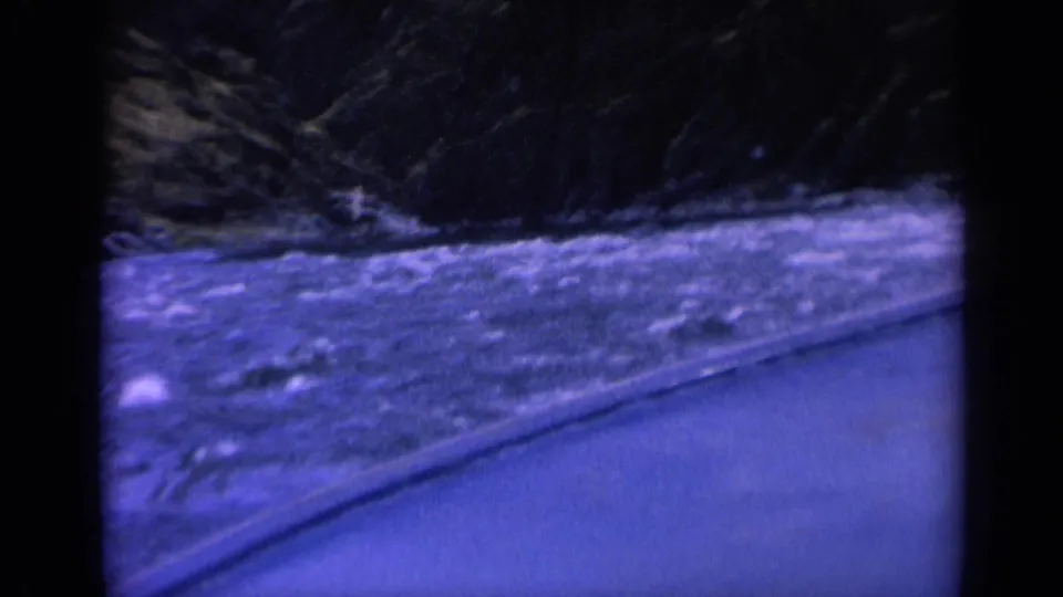 1963 Washington 8mm frame showing river rapids and a curved roadside edge in a dim wooded mountain setting.