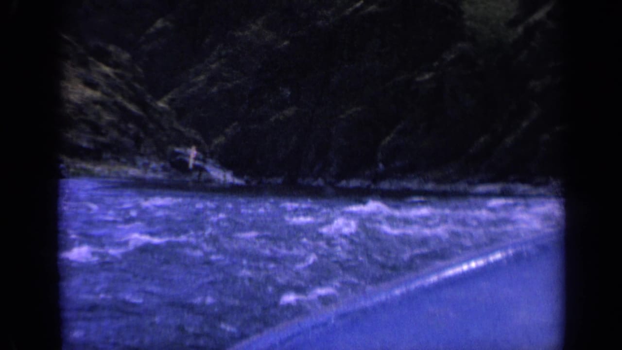 1963 Washington 8mm frame showing turbulent river water, a dark rocky bank, and the curved edge of a small boat in low light.