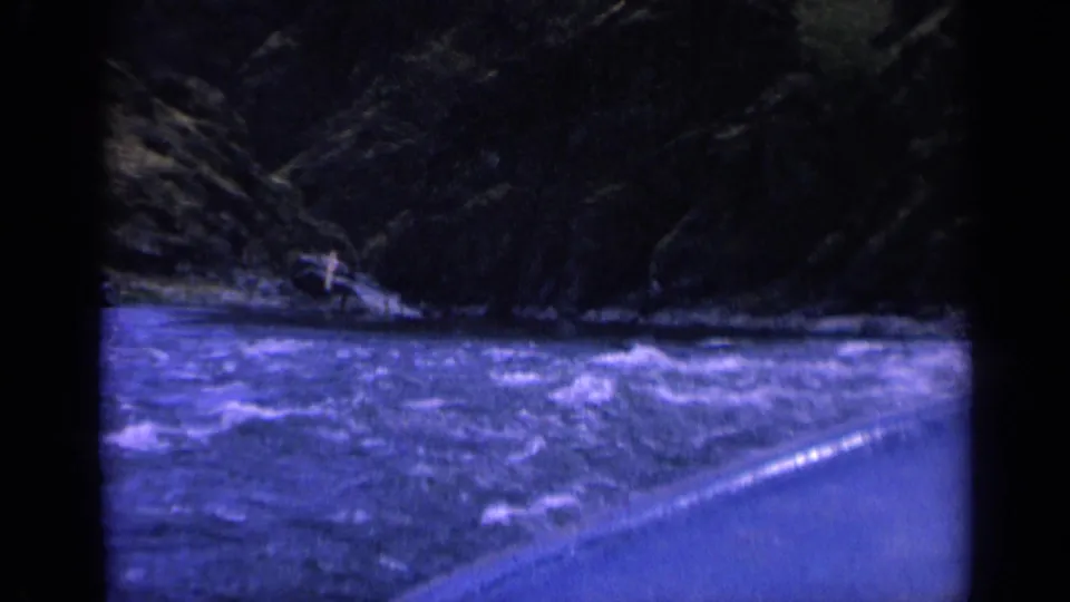 1963 Washington 8mm frame showing turbulent river water, a dark rocky bank, and the curved edge of a small boat in low light.