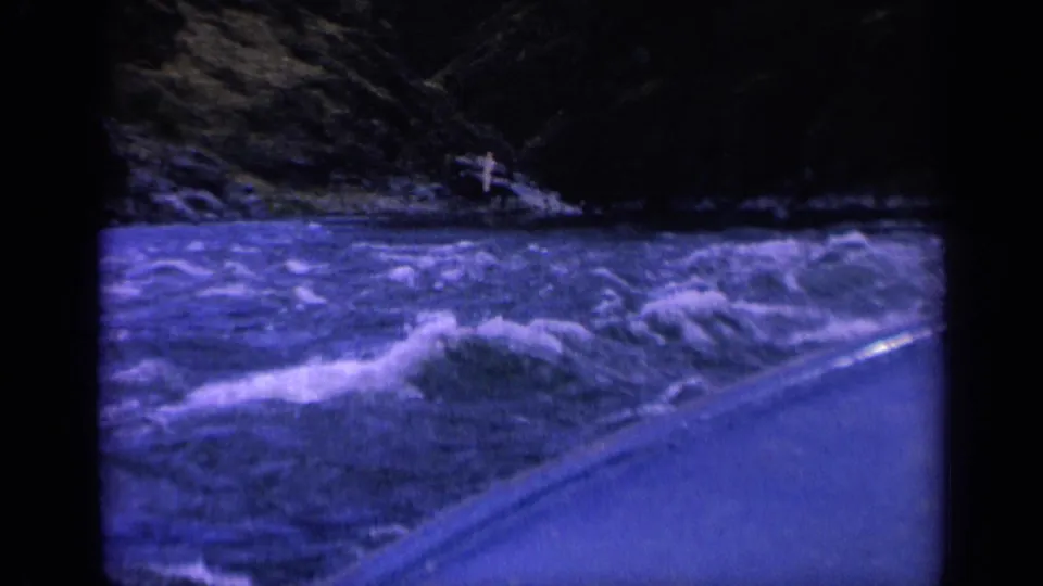 Low-light 8mm frame from Washington in 1963 showing rough river rapids, white spray, and the curved side of a boat.