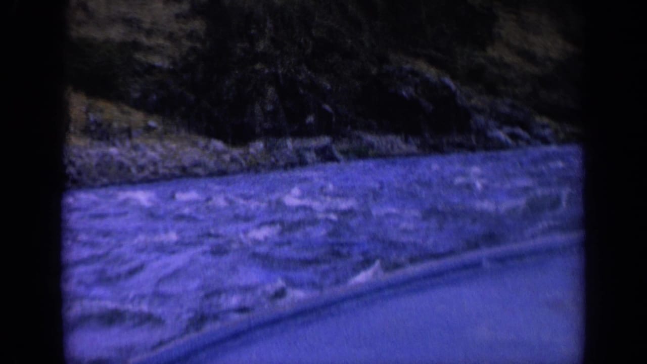 1963 Washington 8mm frame showing rough water beside a boat edge, with a dark rocky shoreline in the background.