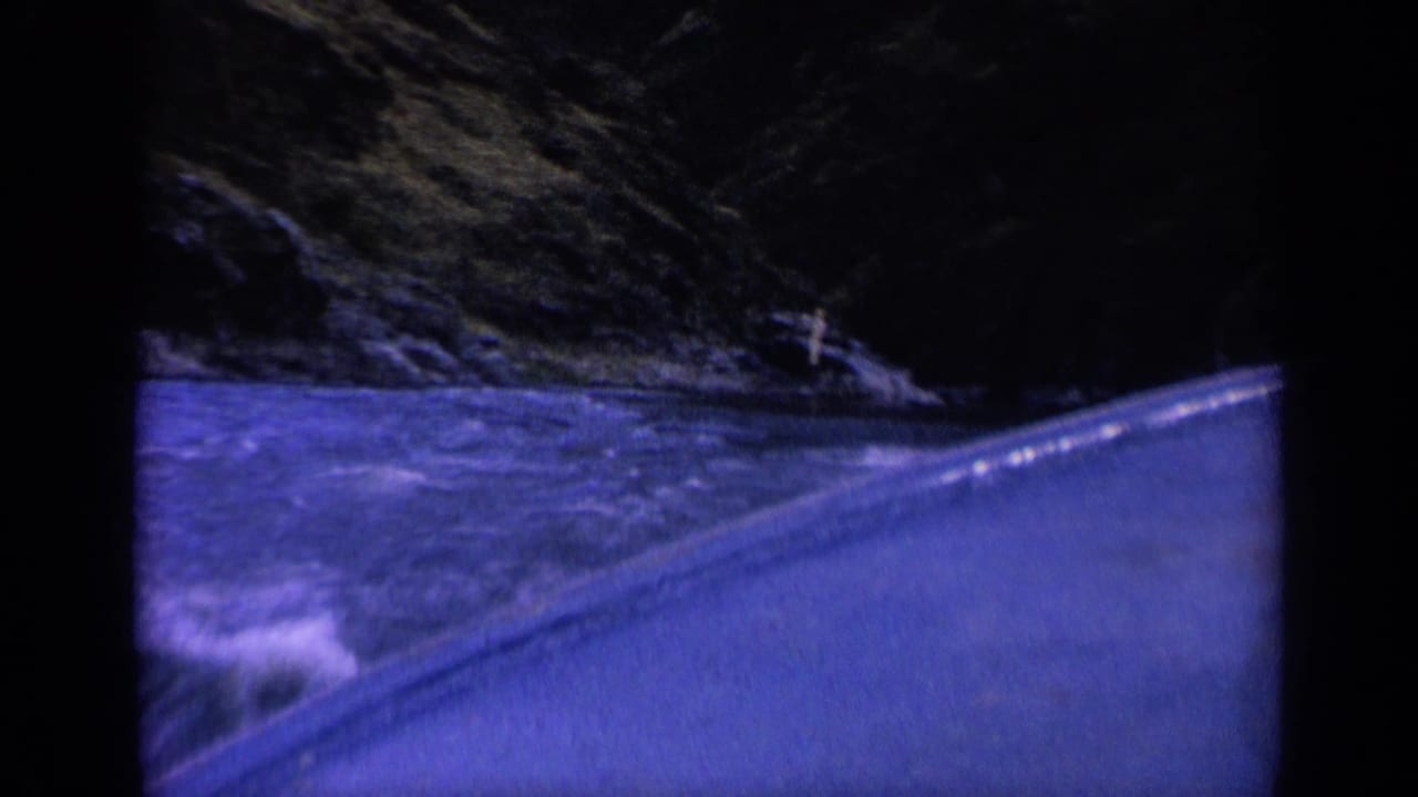 Boat edge cutting through rough water near a dark rocky bank.