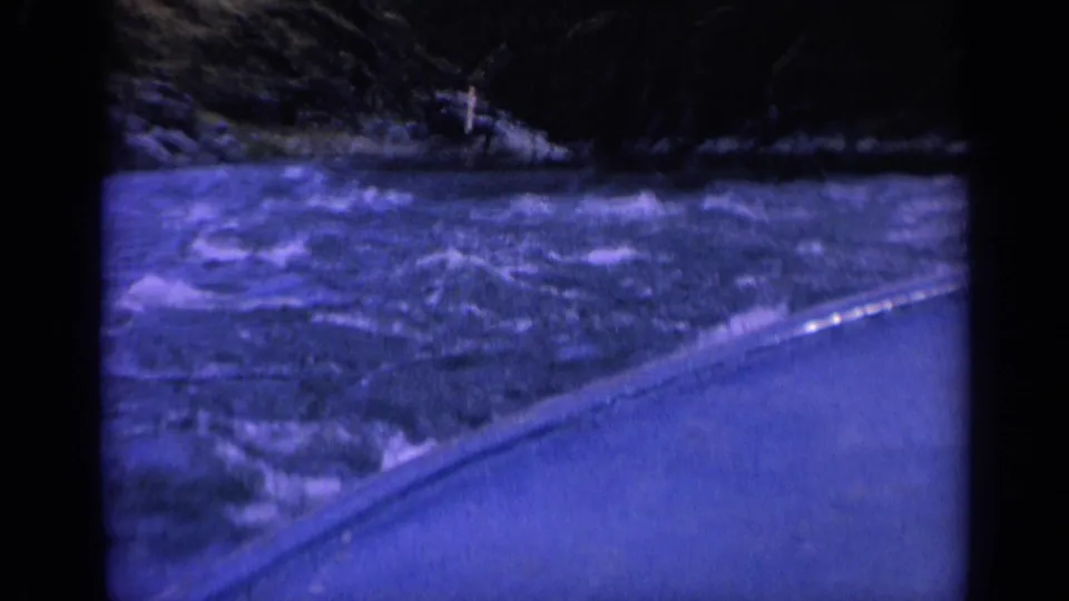 1963 Washington 8mm frame showing foamy, choppy water beside the boat and a dark shoreline beyond.