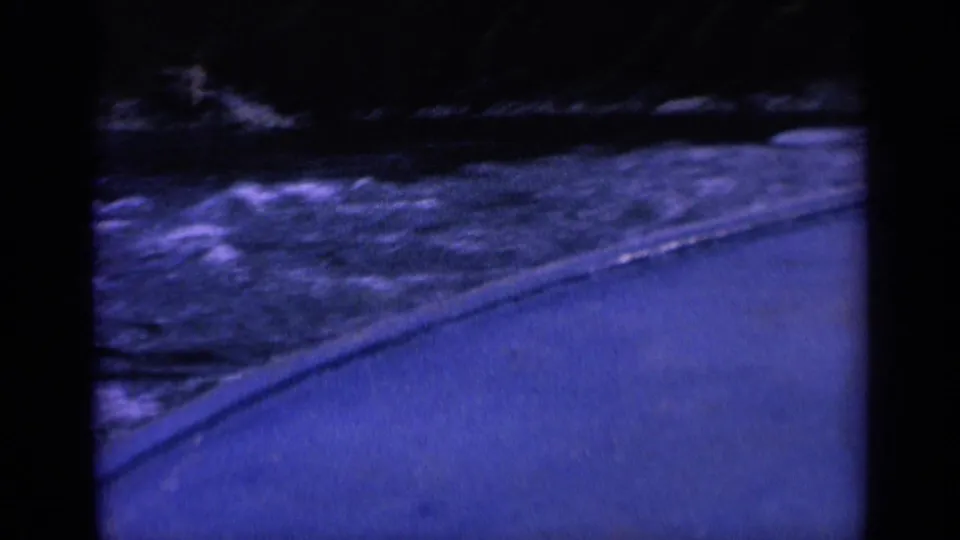 1963 8mm Washington footage shows a boat-level view of rough river water, foam, a paved edge, and shadowed shore.