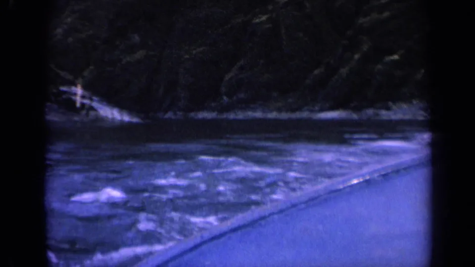 1963 Washington 8mm view from a boat on a river, with rippling water, dark hillside, and the vessel edge in the foreground.