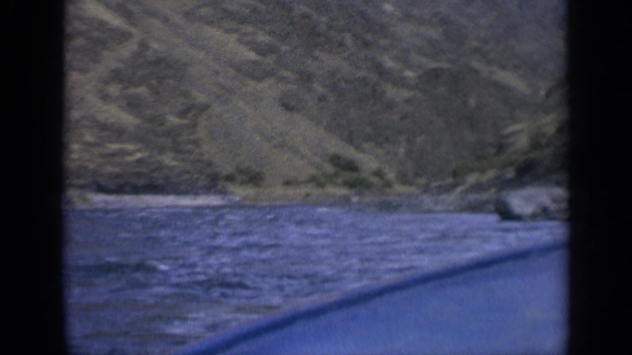 1963 Washington home-movie frame with churning river water, rocky hillside, and a blue boat or canoe edge crossing the foreground.