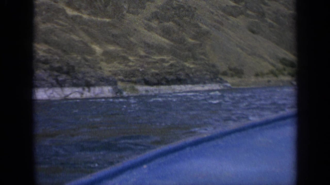 Blue boat edge passes choppy water beside a rocky mountain shoreline.