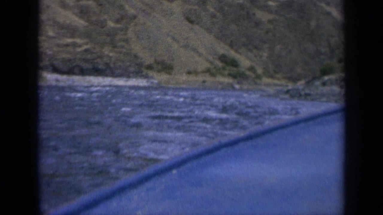 Blue boat edge moving beside rippling river water and a steep hillside.