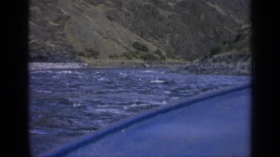 Boat-level view on a Washington river, with the blue hull in the foreground and hillside terrain across the water.