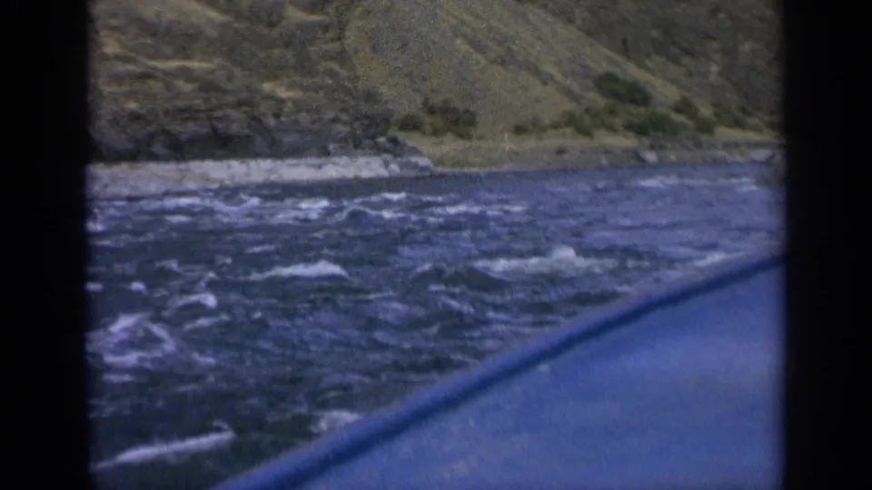 Washington river travel view with the boat edge in the foreground, active ripples on the water, and a steep bank beyond.