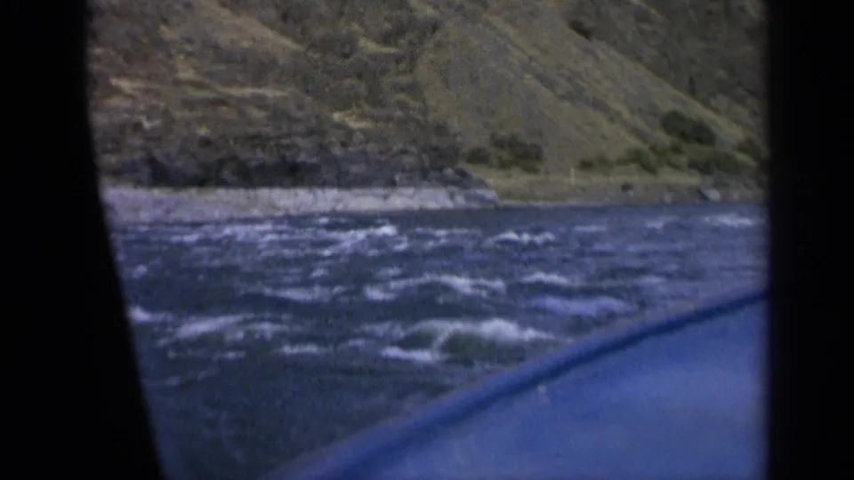 1963 Washington 8mm view from a boat as choppy blue water passes below a rugged grassy bank.