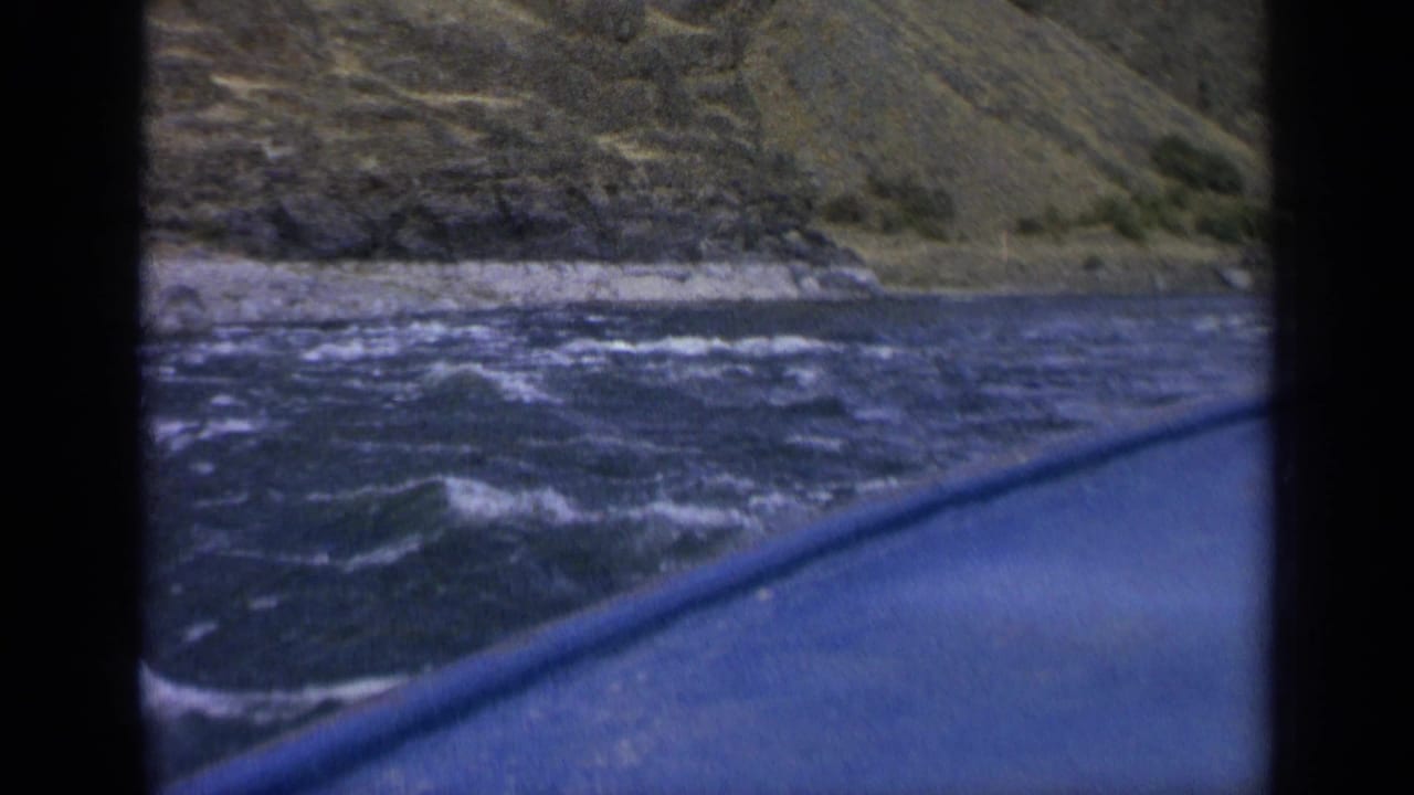 A 1963 Washington home-movie frame shows the boat edge angled across rough water near a sloping rocky bank.