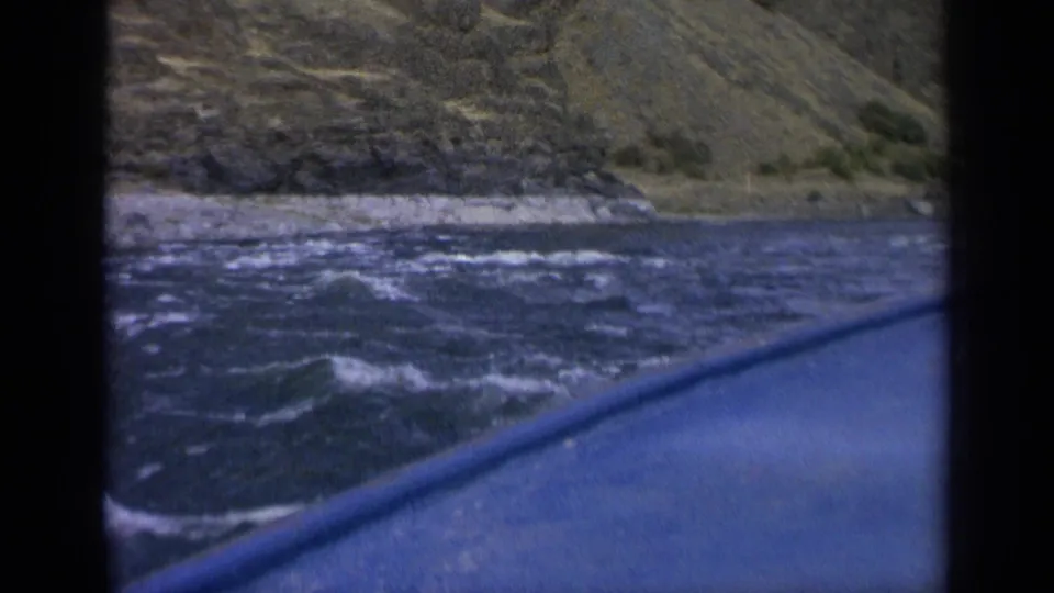 A 1963 Washington home-movie frame shows the boat edge angled across rough water near a sloping rocky bank.