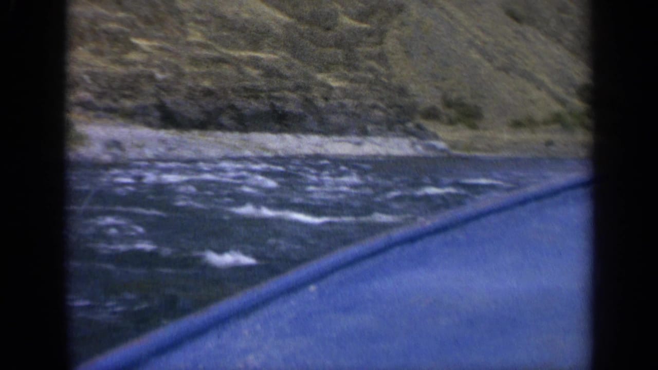 Final frame of a 1963 Washington boat ride with blue hull edge, rippled water, and a rugged shoreline.