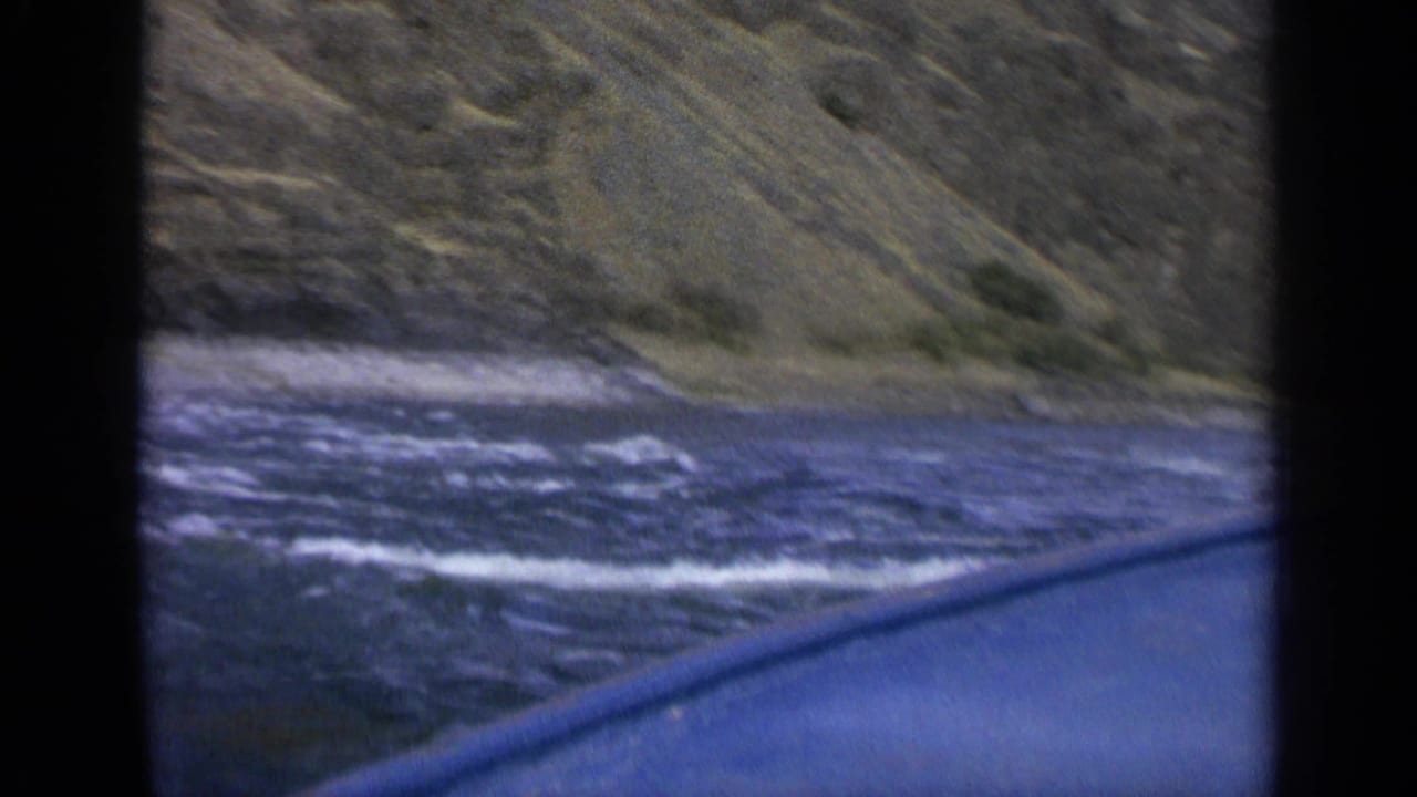 Blue-green river and rocky mountain slope seen past a dark car-window edge.