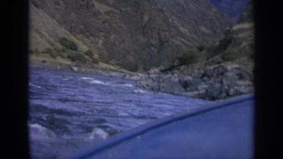 1963 Washington travel footage frame with river rapids, rocky shoreline, and mountain terrain viewed from a vehicle.