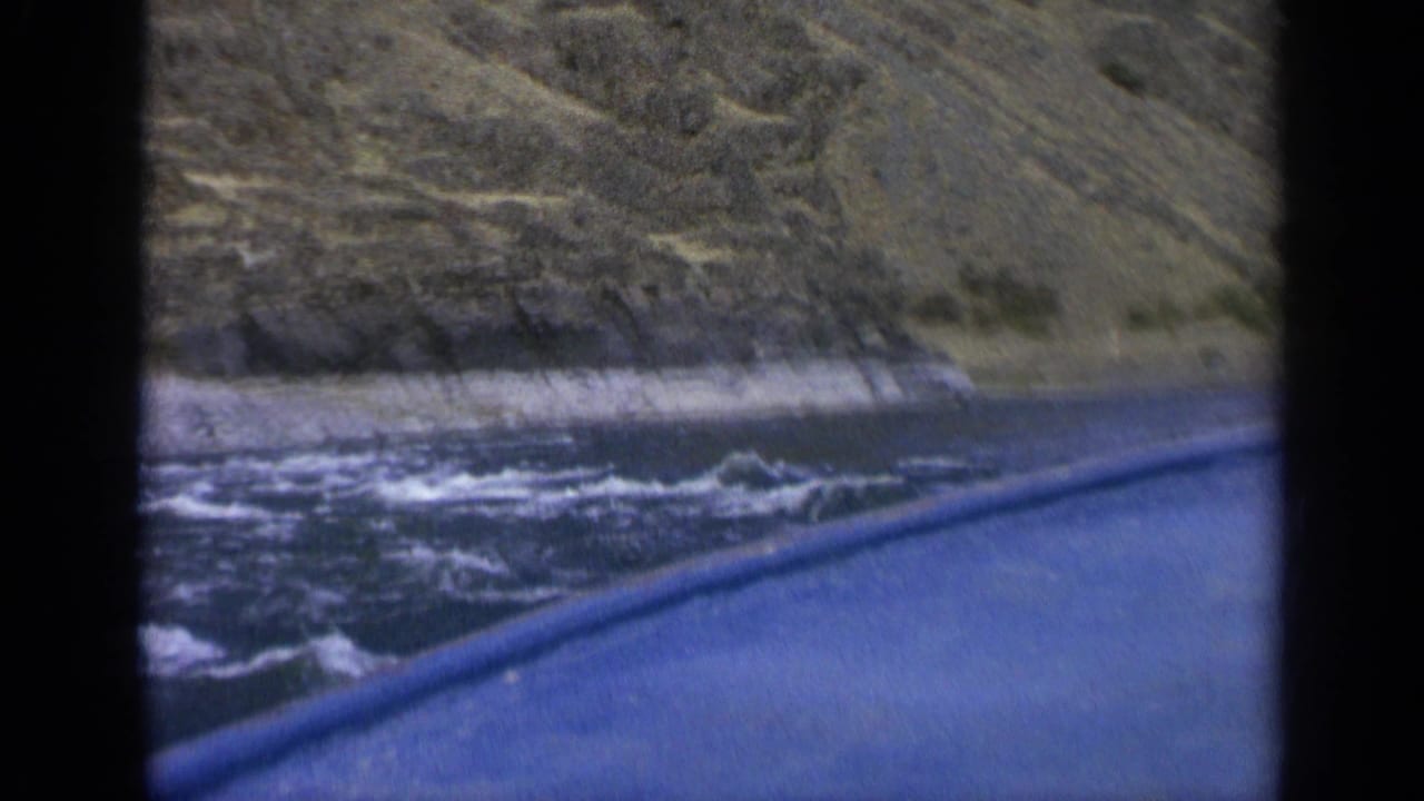 Boat edge beside choppy river water and a steep rocky hillside.