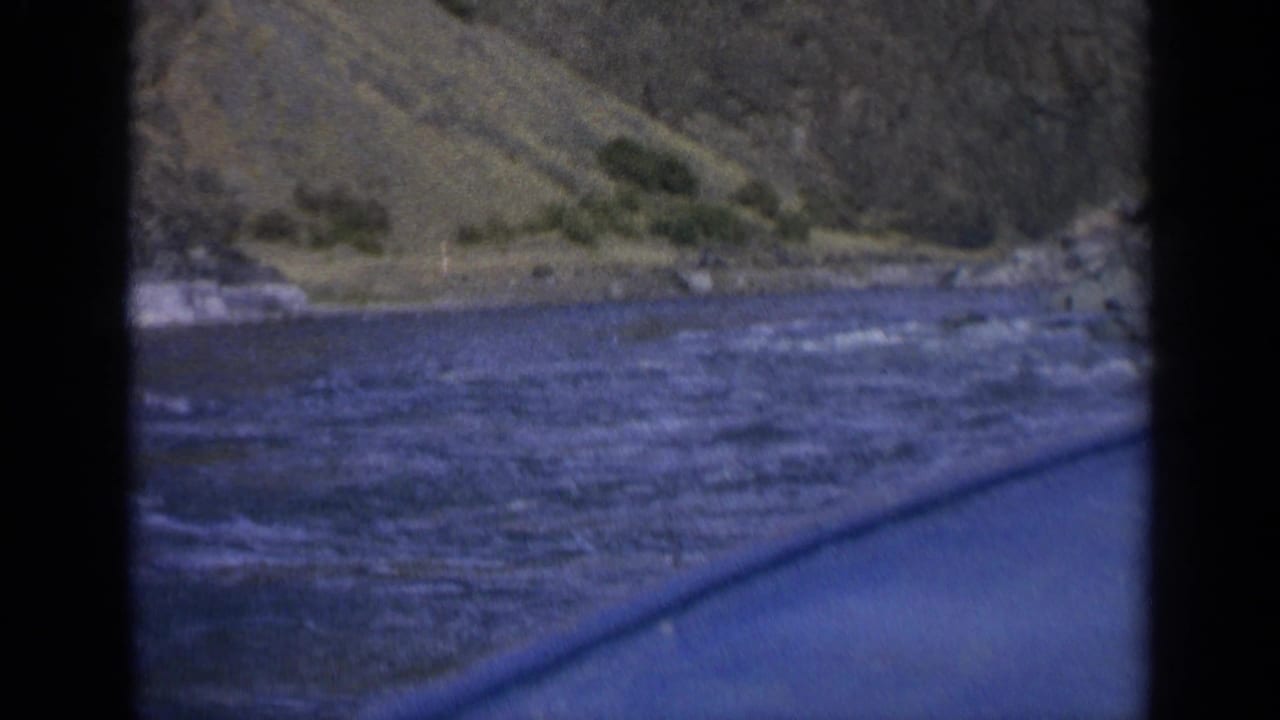 Final 8mm frame showing choppy Washington river water, a low shoreline, sparse vegetation, and the boat edge in foreground.